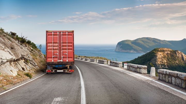 Truck carrying a shipping container along a coastal road